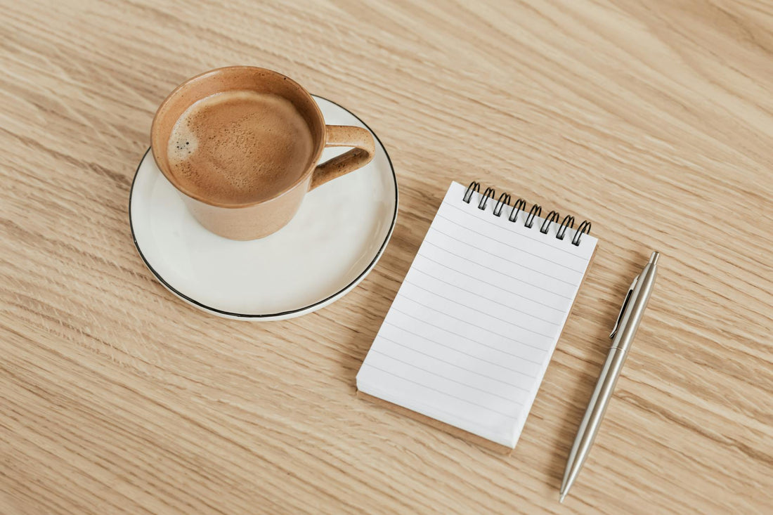 Morning coffee journaling setup with mug, spiral notepad, and pen on a wooden table
