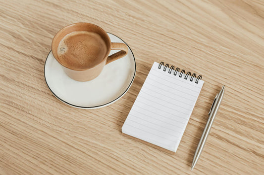 Morning coffee journaling setup with mug, spiral notepad, and pen on a wooden table