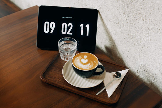 Latte and water beside a large digital clock, signaling best time to drink coffee