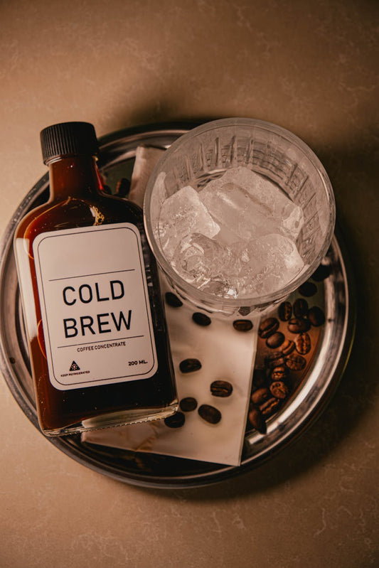Cold brew coffee over ice in a clear glass with coffee beans on a wooden table